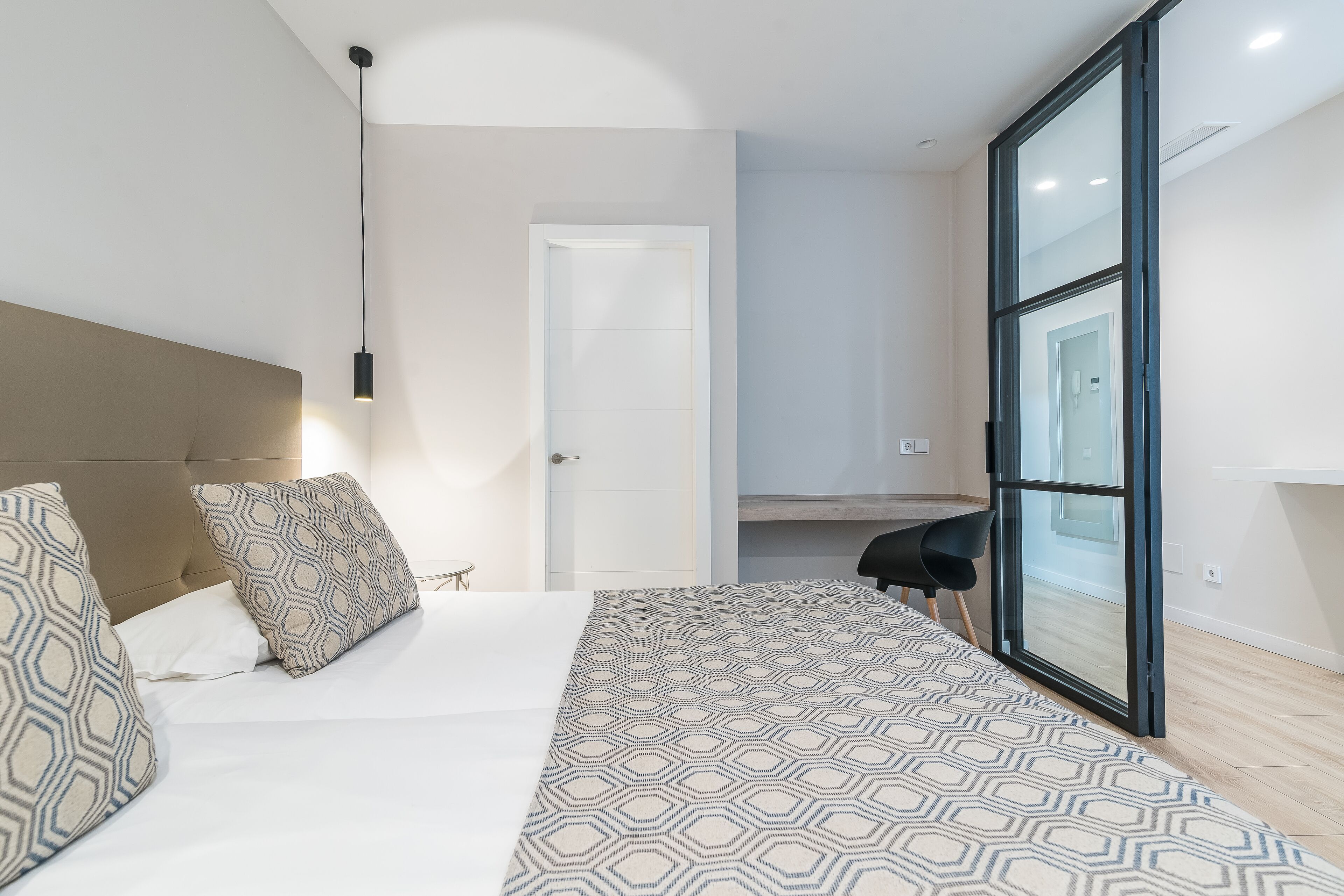 Un dormitorio moderno con una cama grande, ropa de cama con estampado geométrico, cabecera y vistas a través de un ventanal.