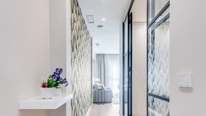 A modern hallway with a white shelf holding plants, a patterned wall, and a view into a room with a bed and a window.