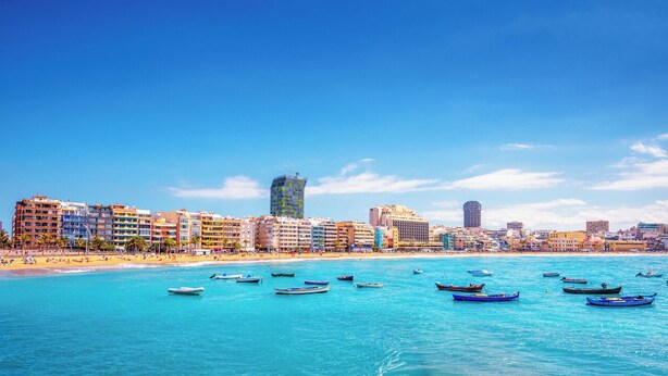 A coastal cityscape with a beach, numerous boats, and a variety of buildings including hotels.