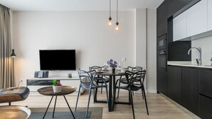 A modern kitchen with dark cabinetry, a built-in oven, and a large flat-screen TV mounted on the wall.