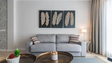 Ein modernes Wohnzimmer mit grauem Sofa, dekorativer Federwandgestaltung, einer kleinen Topfpflanze und einem runden Couchtisch.