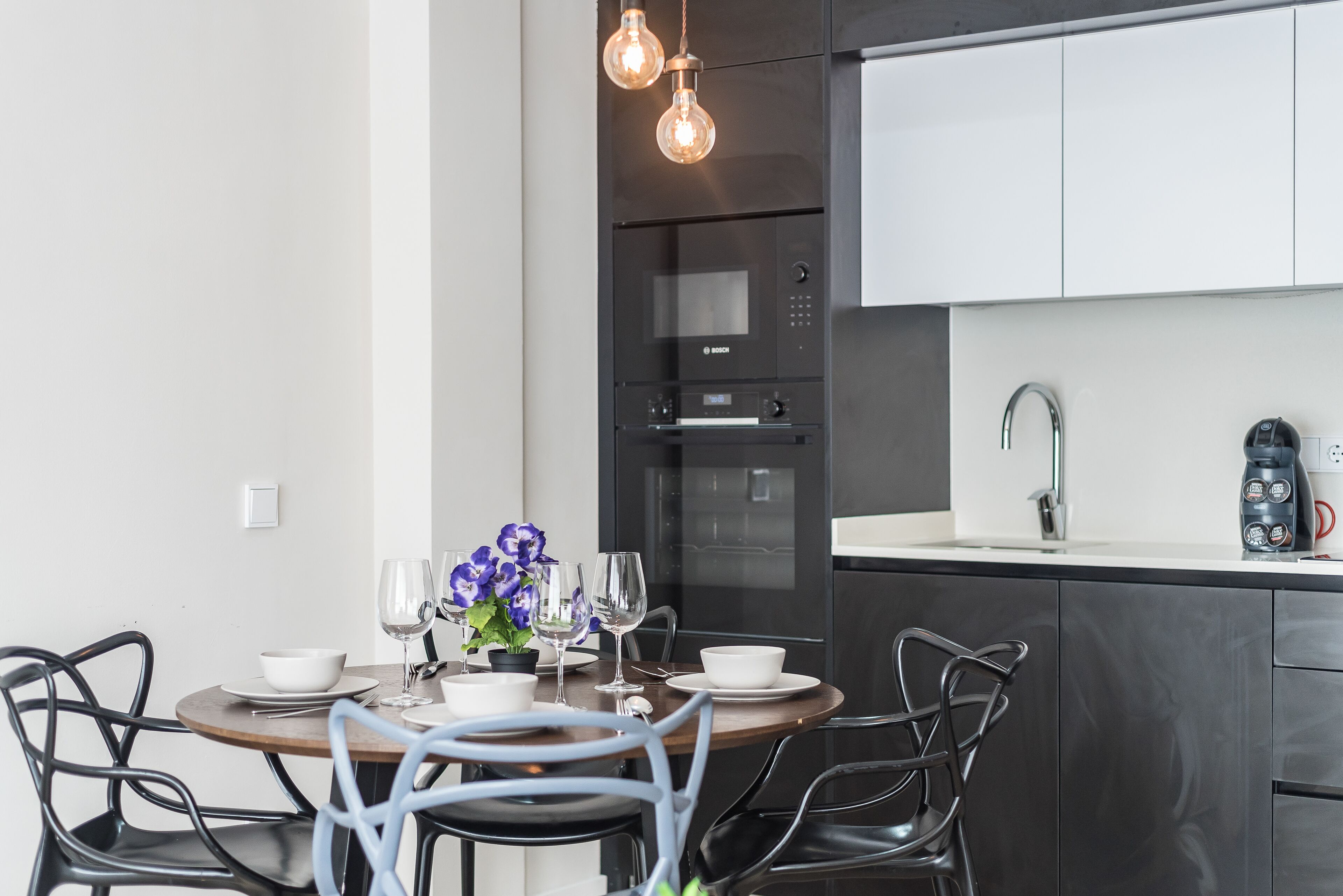 A modern kitchen with a built-in oven and microwave, a dining table with chairs, and a hanging light fixture.