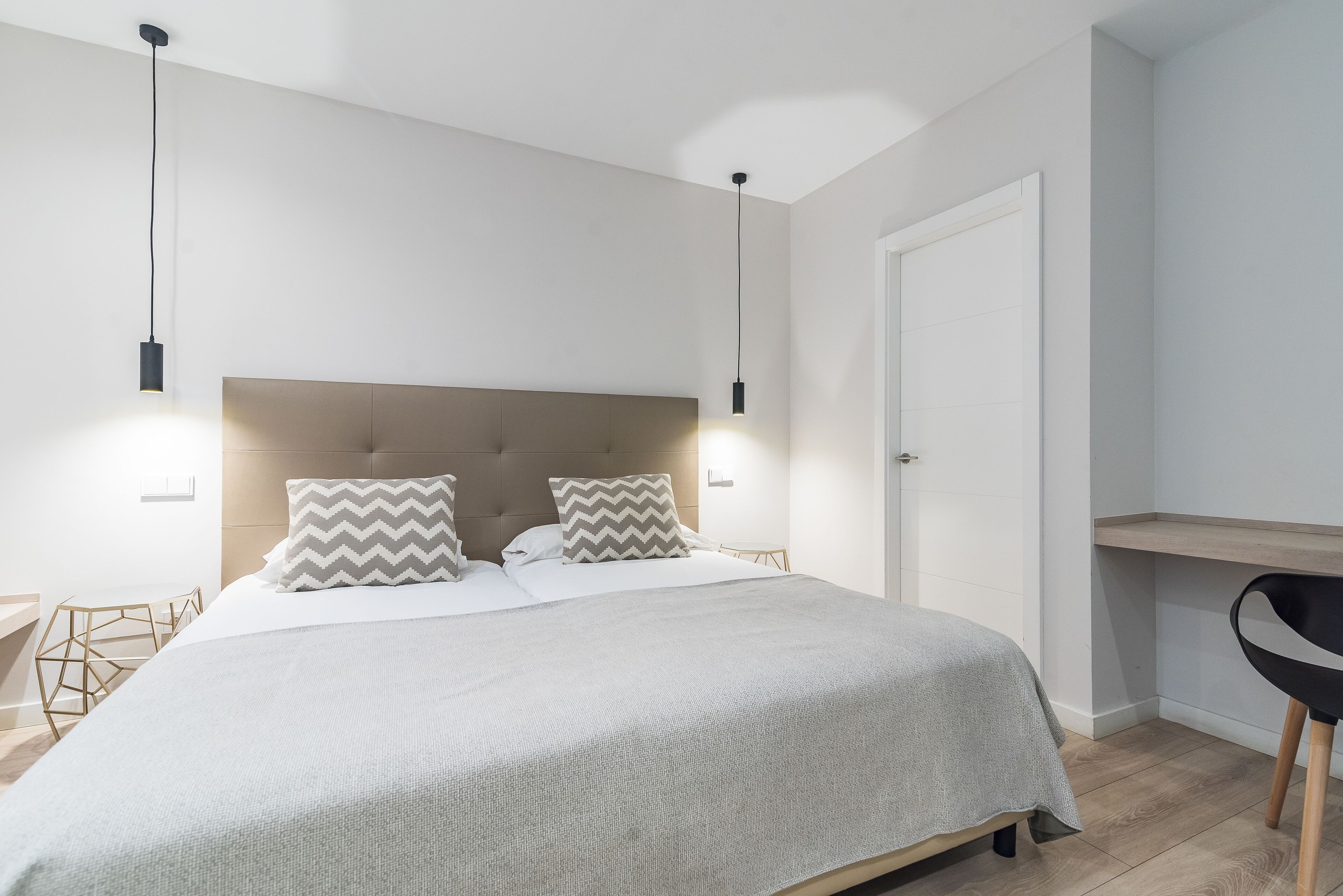 Un dormitorio moderno con una cama grande, dos lámparas de noche, un cabecero de madera y un escritorio con una silla.