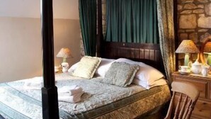 Una cama con dosel y cortinas verdes, una pared de piedra y dos lámparas de noche.