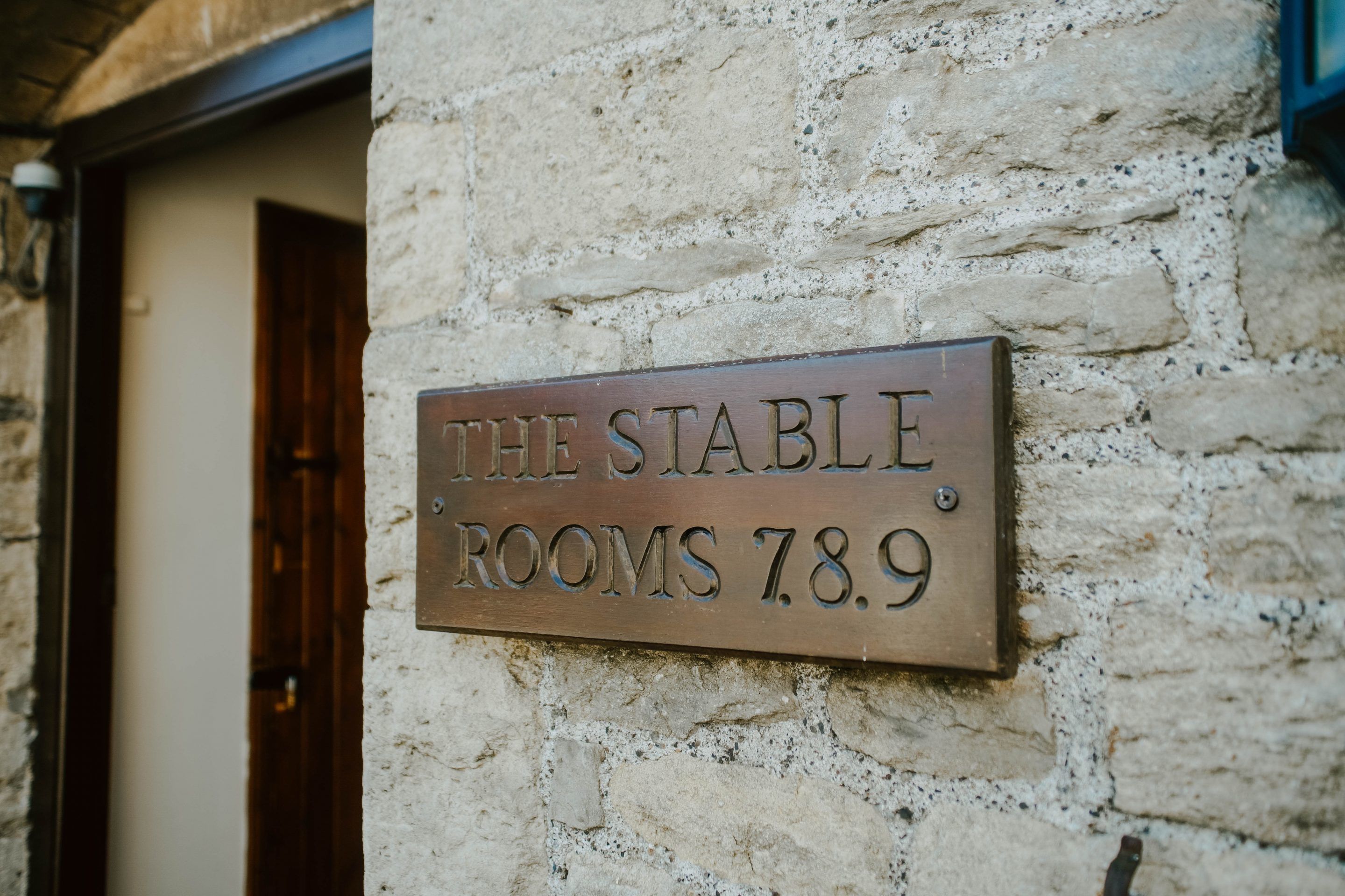 A sign on a stone wall indicating "The Stable Rooms 7.8.9".