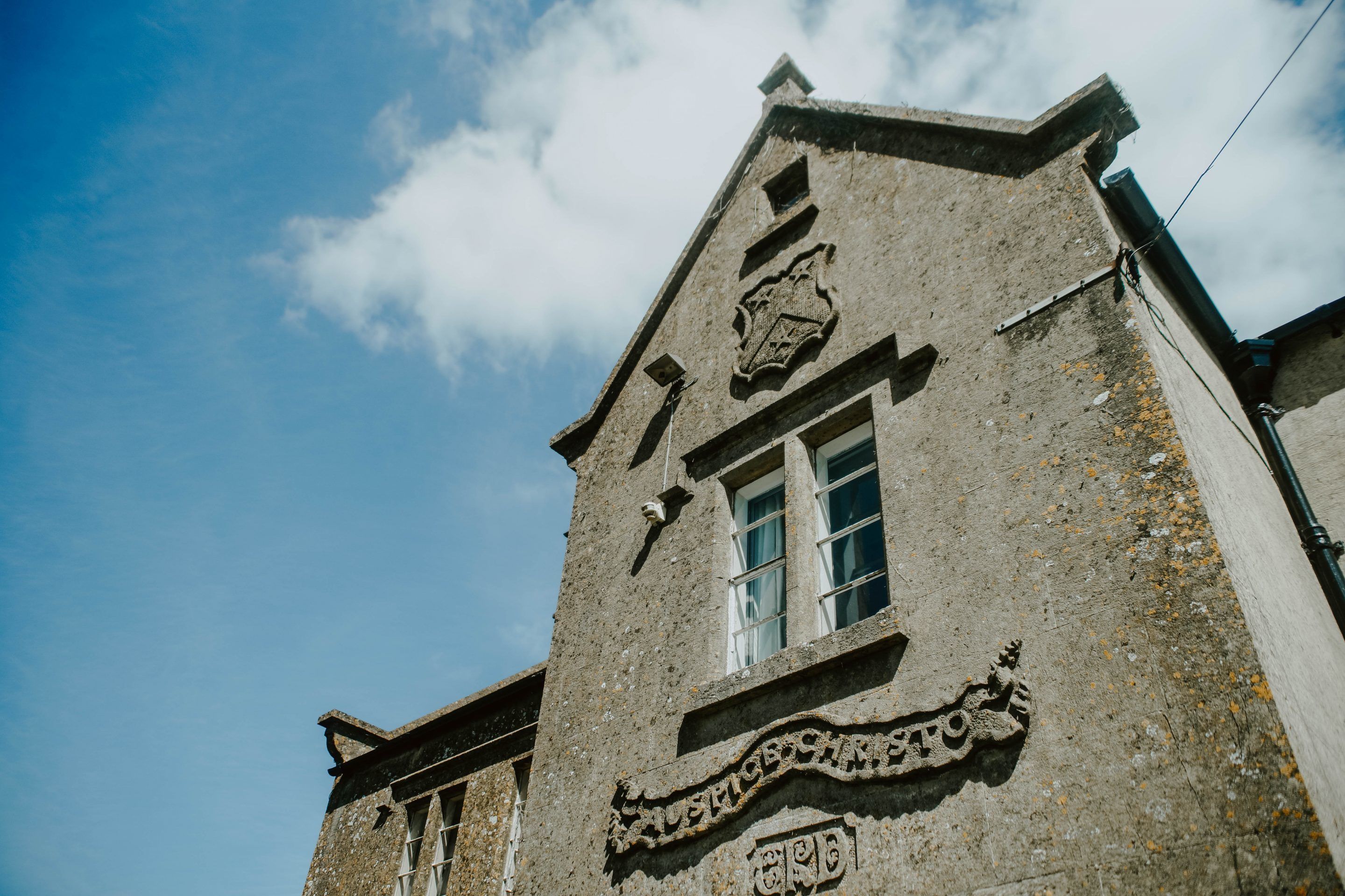 A historic building with a stone facade, a prominent crest, and a window with a grid pattern.