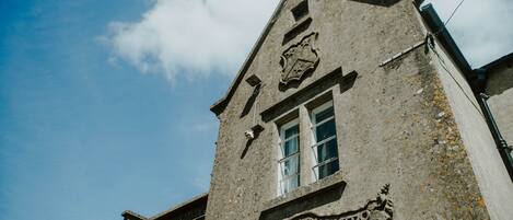 A historic building with a stone facade, a prominent crest, and a window with a grid pattern.