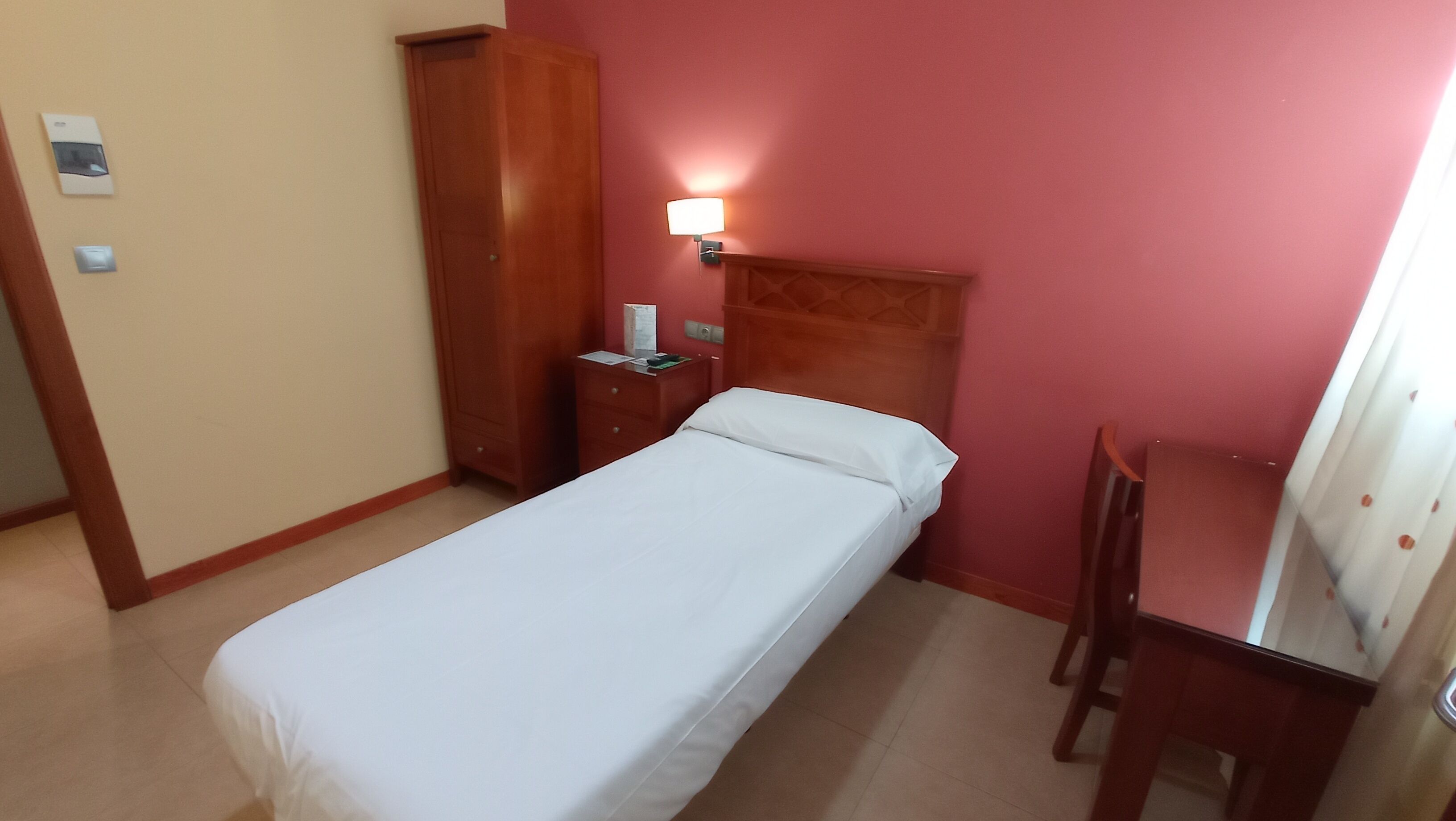 Une petite chambre à coucher, bien rangée, avec un lit simple, une armoire en bois, une table de chevet et un bureau avec une chaise.