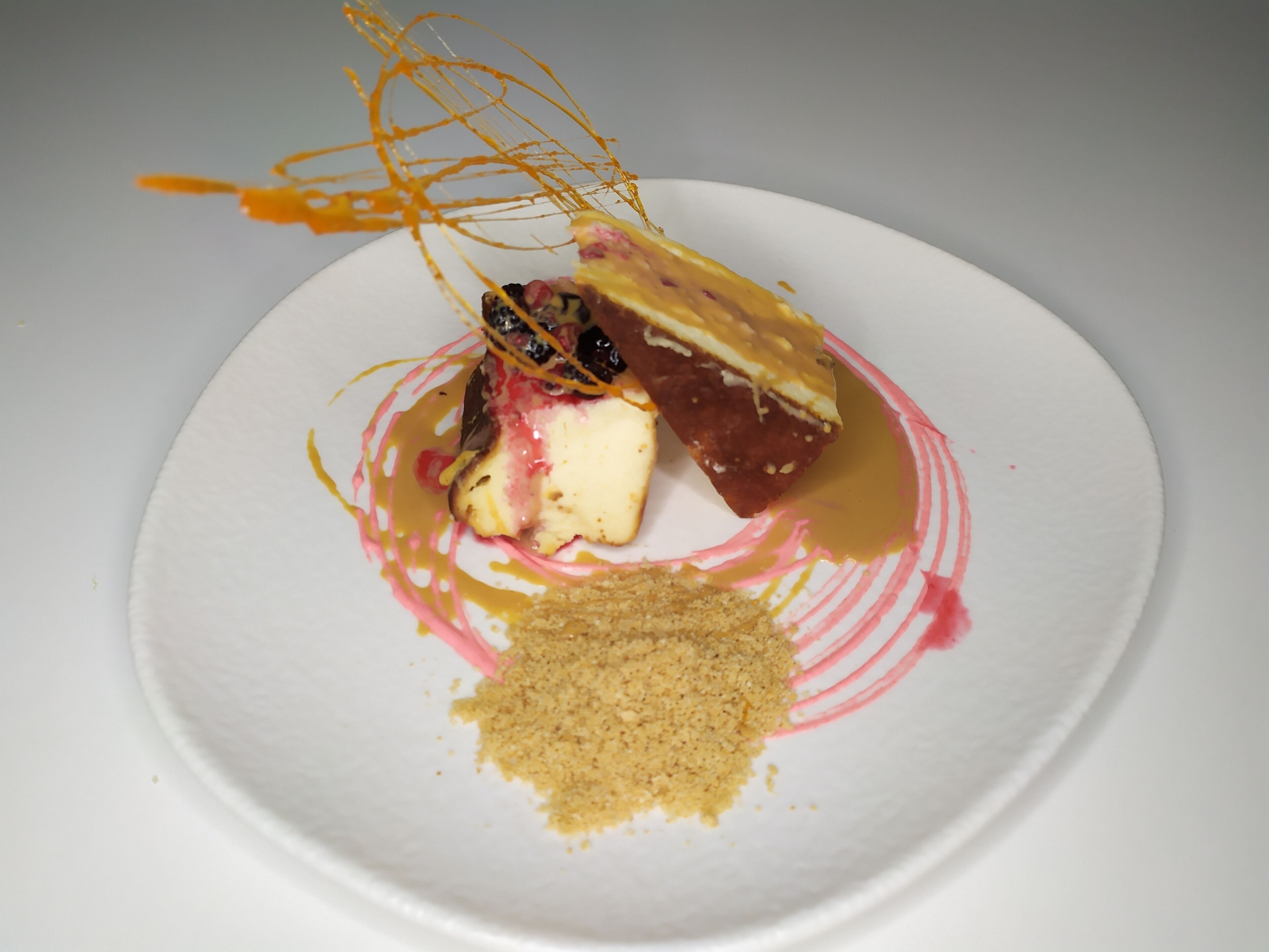 Sobremesa em um prato branco com calda de caramelo e molho rosa.