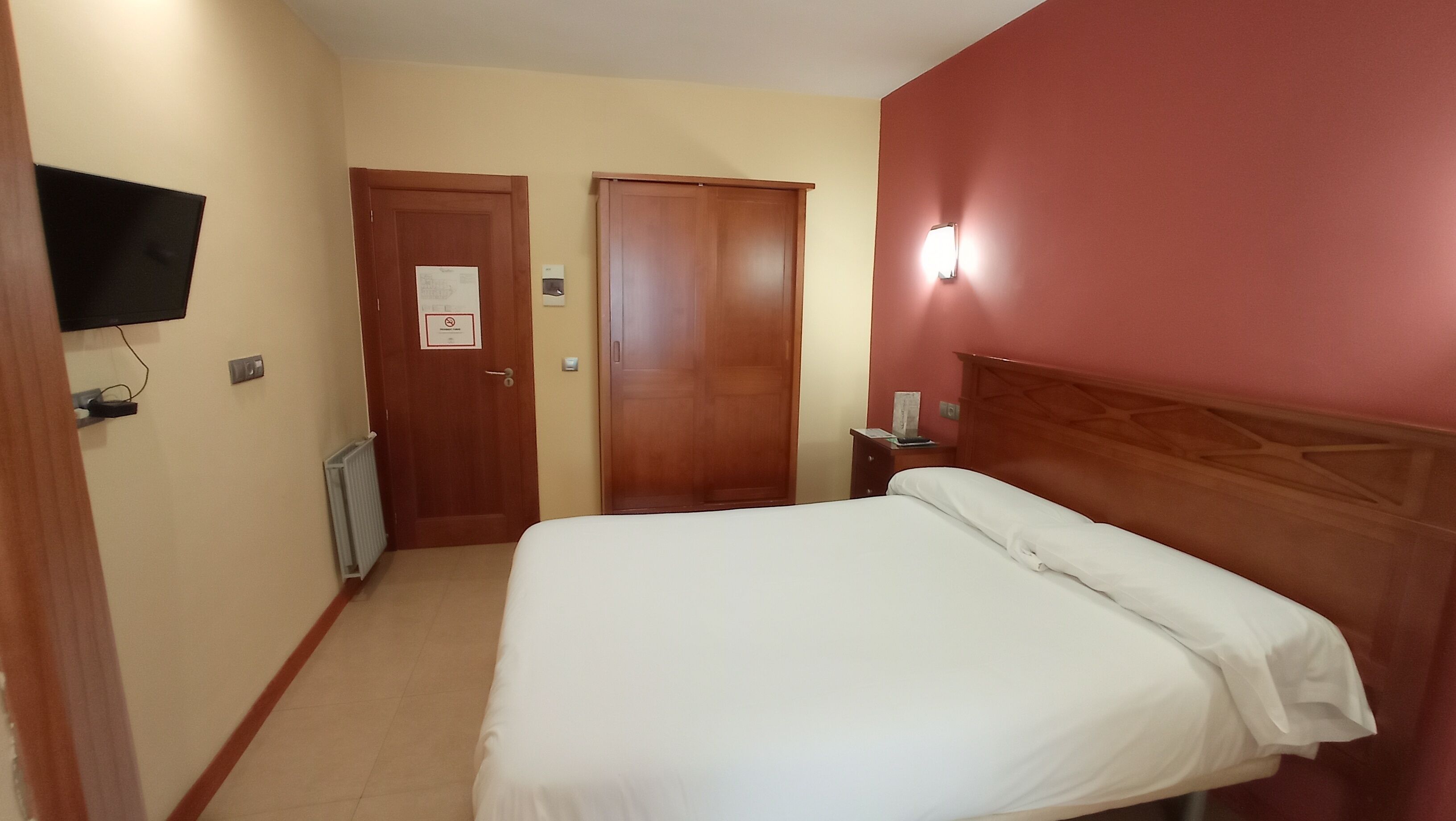 Une chambre d’hôtel avec un lit, un téléviseur fixé au mur et deux portes.