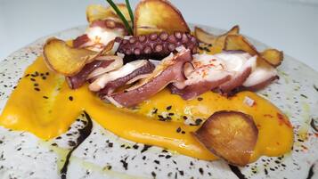 Un plat composé de poulpe, de pommes de terre et d’une sauce jaune, le tout servi dans une assiette à motifs.