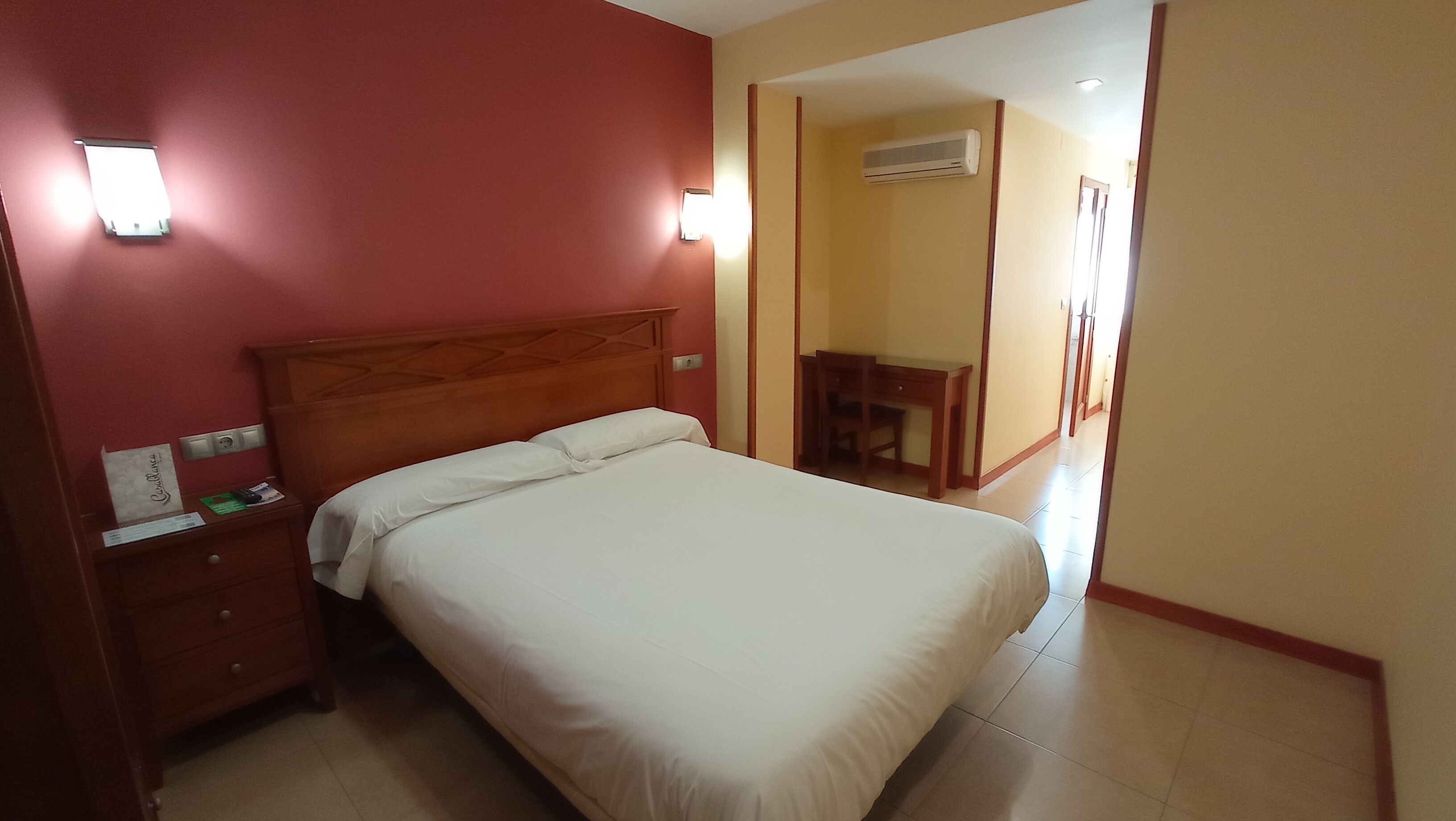 A hotel room with a bed, a nightstand, a desk, and a chair.