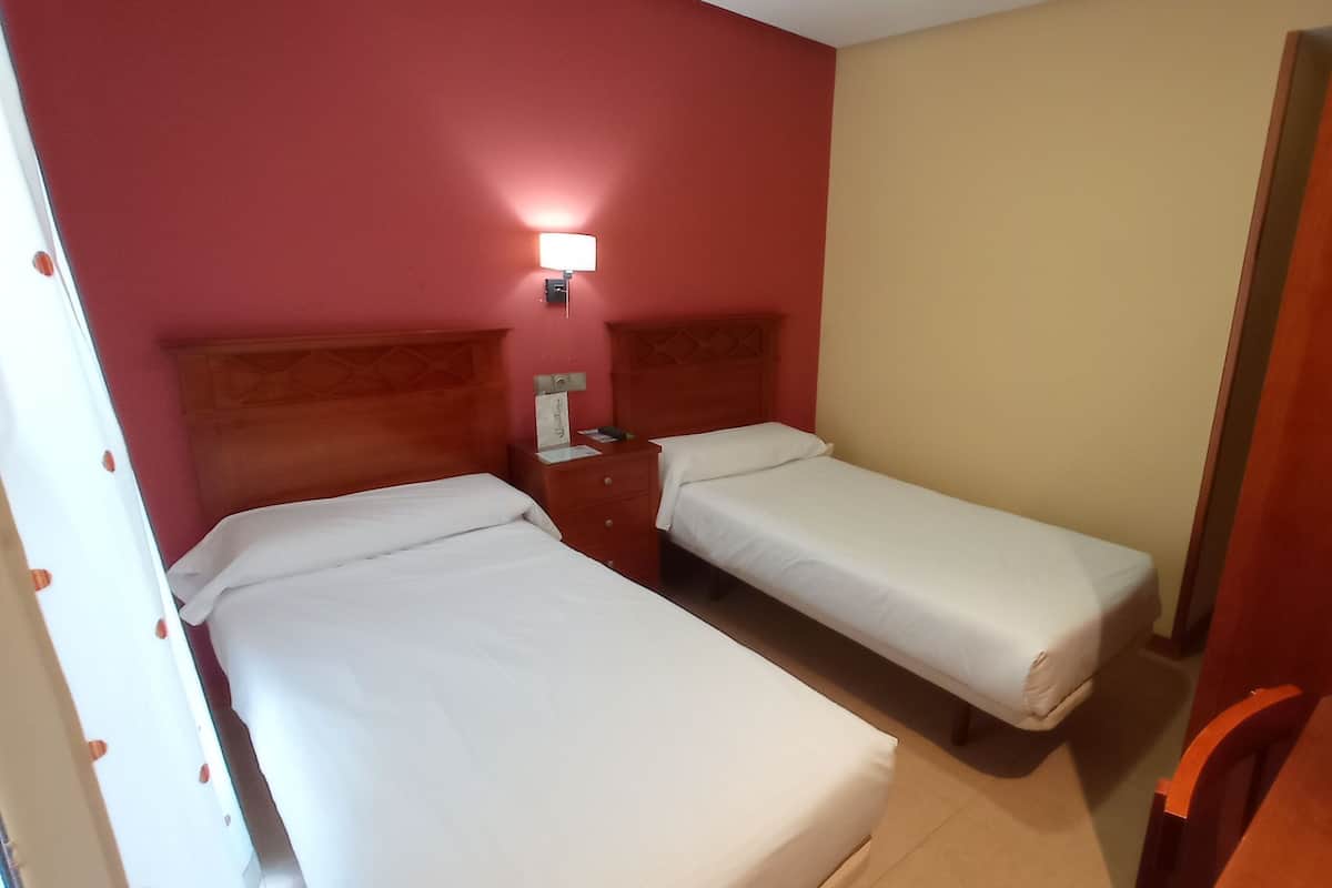 Ein Hotelzimmer mit zwei Einzelbetten, einem Nachttisch, einer Lampe und einem Holzschrank.