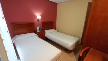 A hotel room with two single beds, a nightstand, a lamp, and a wooden wardrobe.
