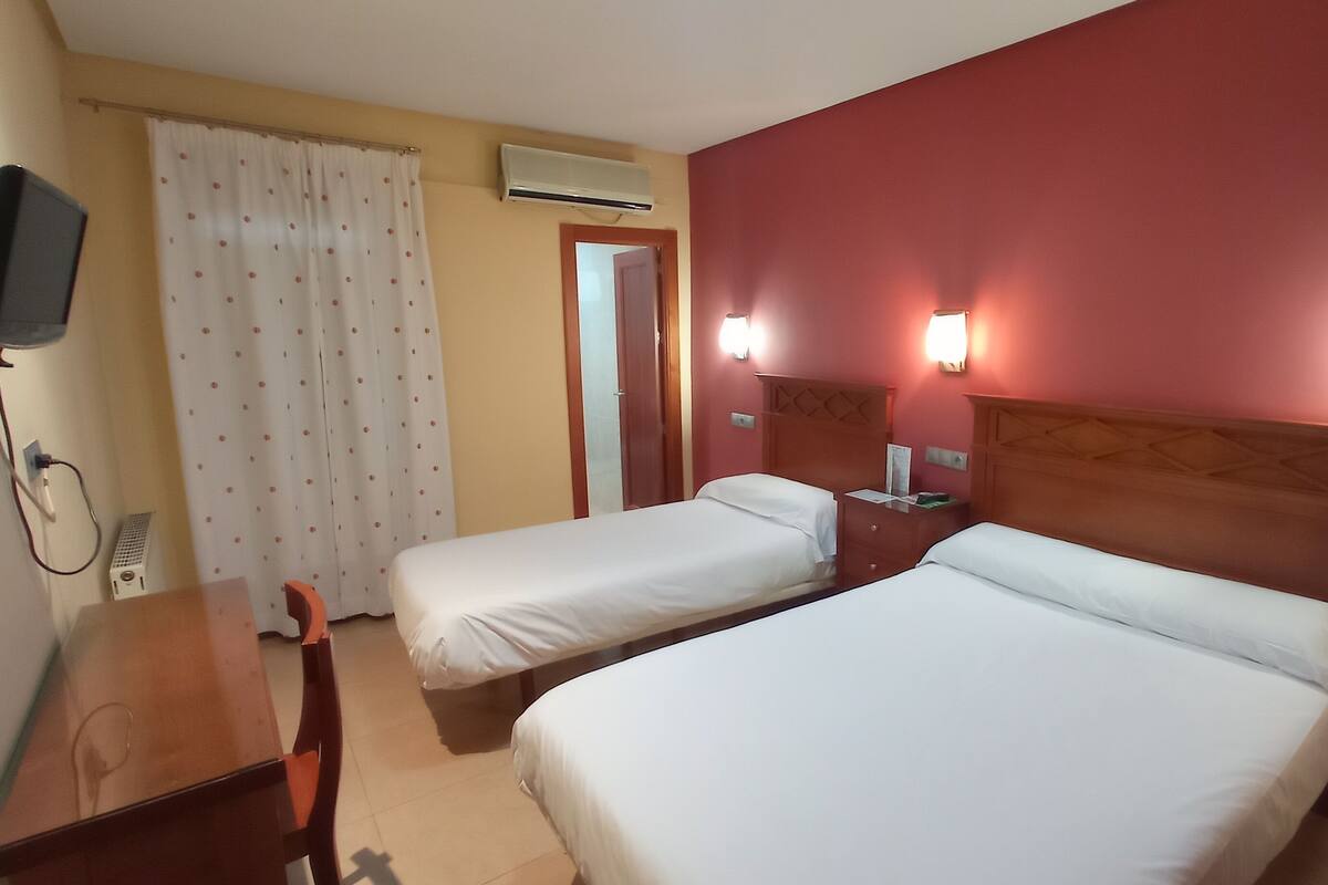 Ein Hotelzimmer mit zwei Einzelbetten, einem Schreibtisch, einem Stuhl, einer Klimaanlage und einem Fernseher.