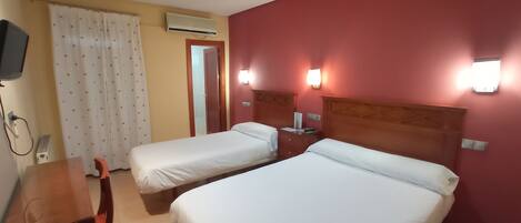 Une chambre d’hôtel avec deux lits simples, un bureau, une chaise, un appareil de climatisation et un téléviseur.