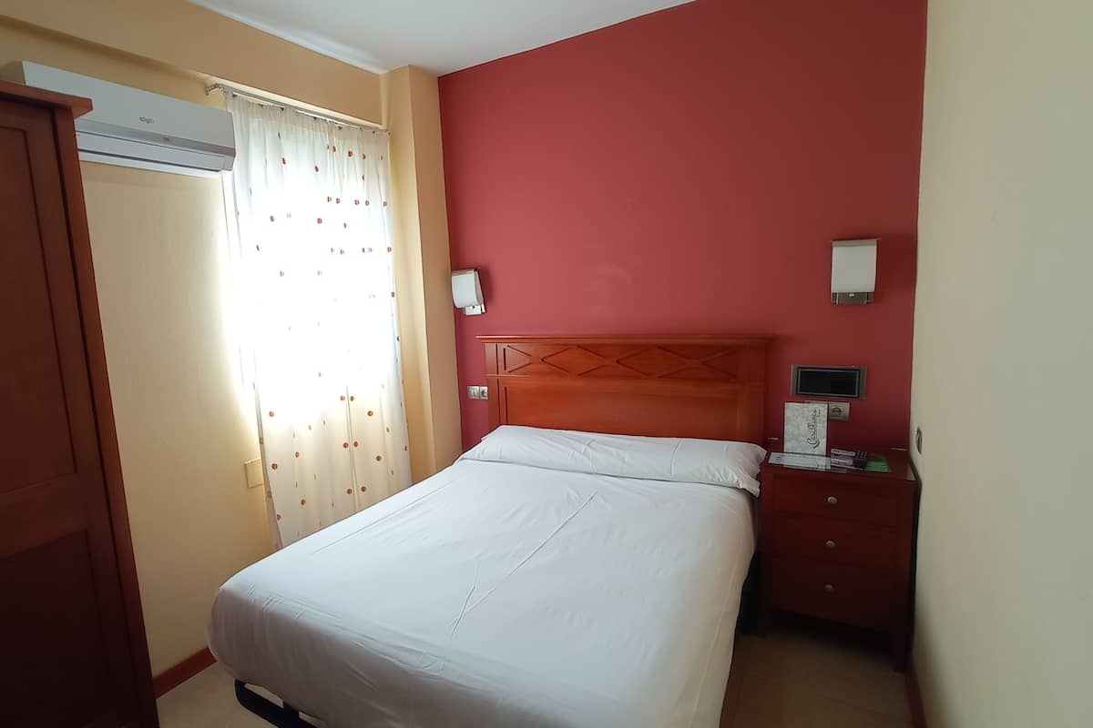 Ein Hotelzimmer mit einem Bett, einem Nachttisch, einem Kleiderschrank und einem Fenster mit Vorhängen.
