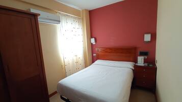 Une chambre d’hôtel avec un lit, une table de chevet, une armoire et une fenêtre avec des rideaux.
