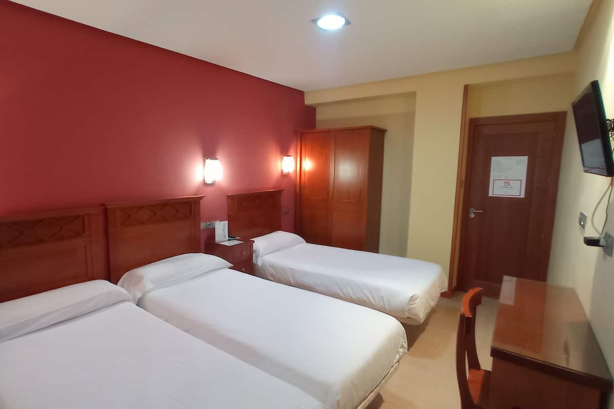 Ein Hotelzimmer mit zwei Einzelbetten, einem Holzschrank, einem Schreibtisch und einem an der Wand befestigten Fernseher.