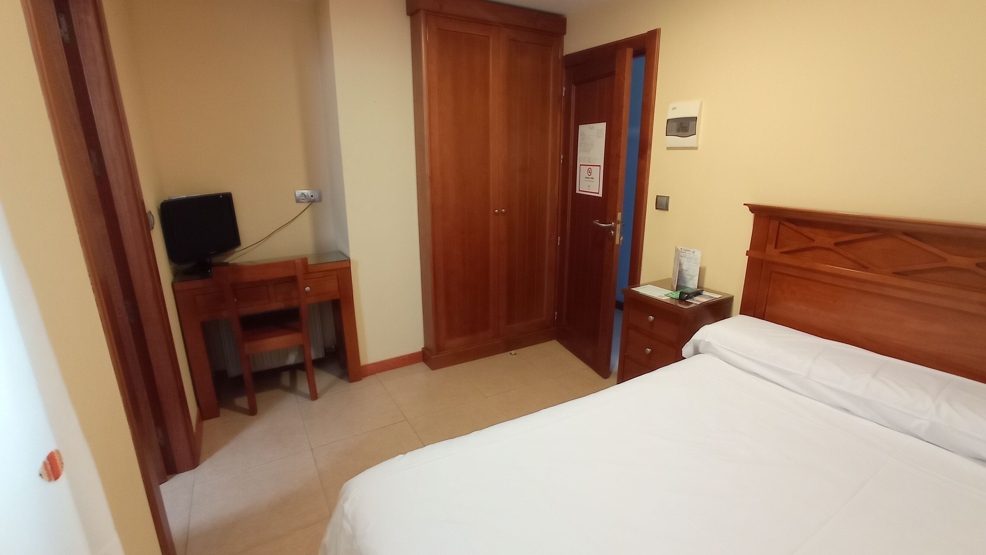Una habitación de hotel con cama, escritorio, televisor y armario.