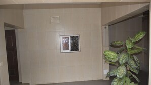 A hallway with beige tiled walls, a potted plant, and a framed picture on the wall. - Résidence Hotel Carmel (Abidjan)