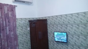 A room with a wooden door, a television mounted on the wall, and patterned wallpaper. - Résidence Hotel Carmel (Abidjan)