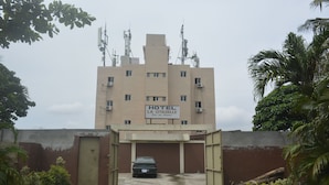 A hotel entrance with a car parked in front, surrounded by greenery and a clear sky. - Résidence Hotel Carmel (Abidjan)