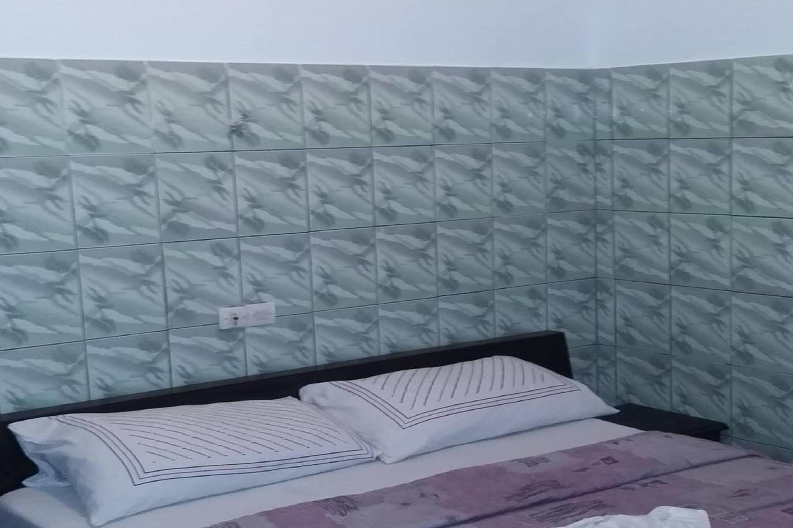 Un dormitorio con pared estampada, una cama con dos almohadas y una mesita de noche.