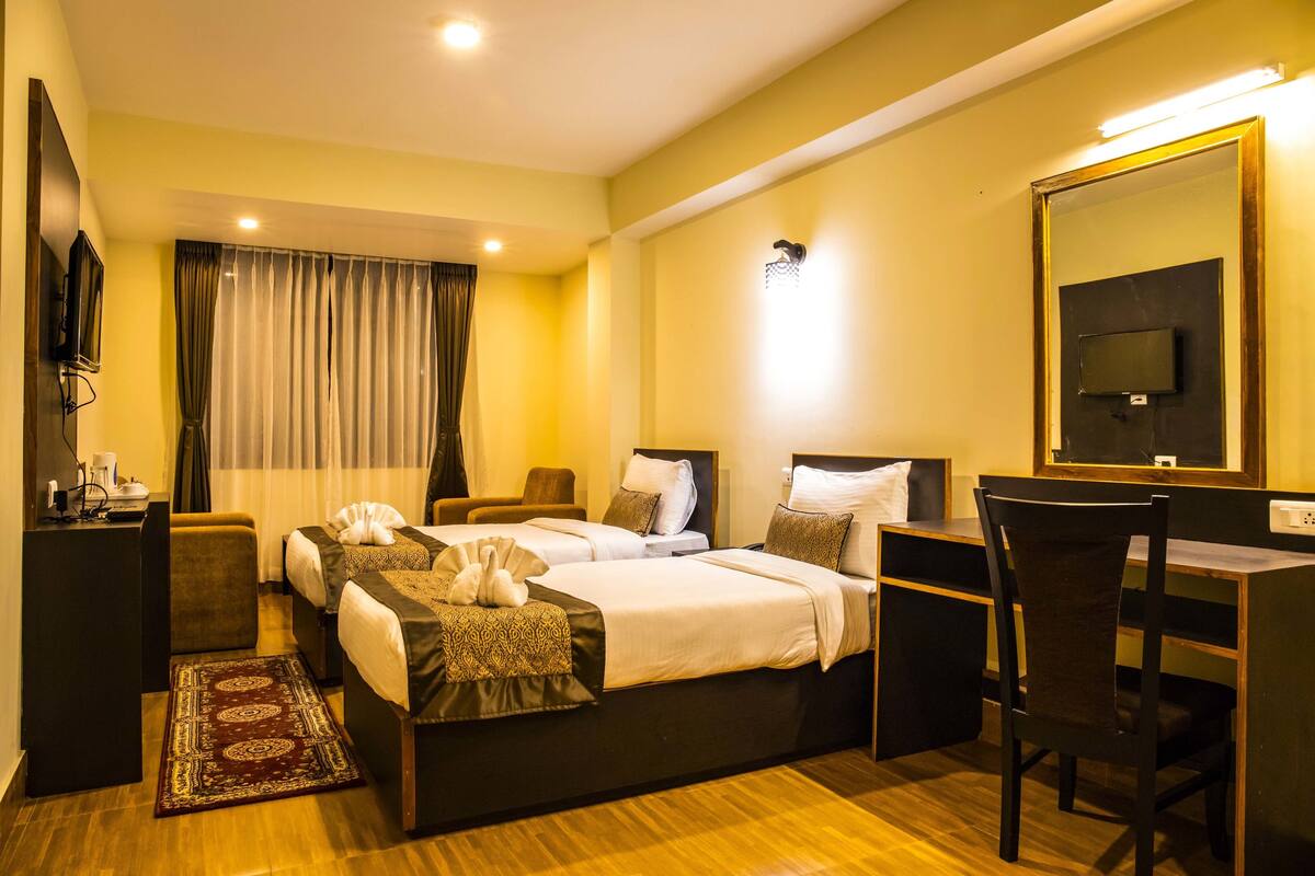 A hotel room with two beds, a desk, a chair, a TV, and a bathroom with a shower and toilet.