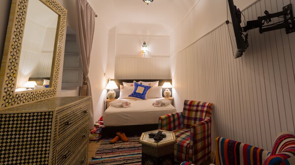 Una habitación de hotel con una cama, dos lámparas de noche, un espejo, un aparador y una silla.