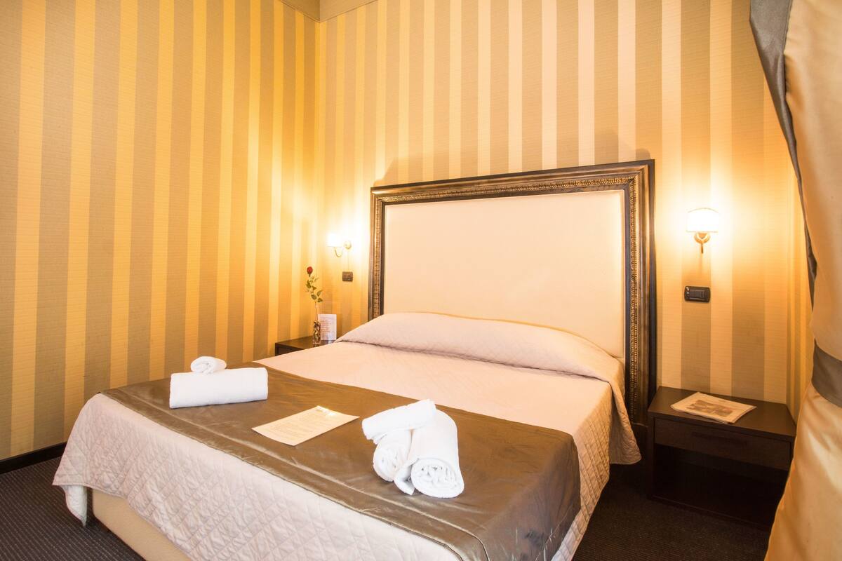 A hotel room with a large bed, two bedside tables, and striped wallpaper.