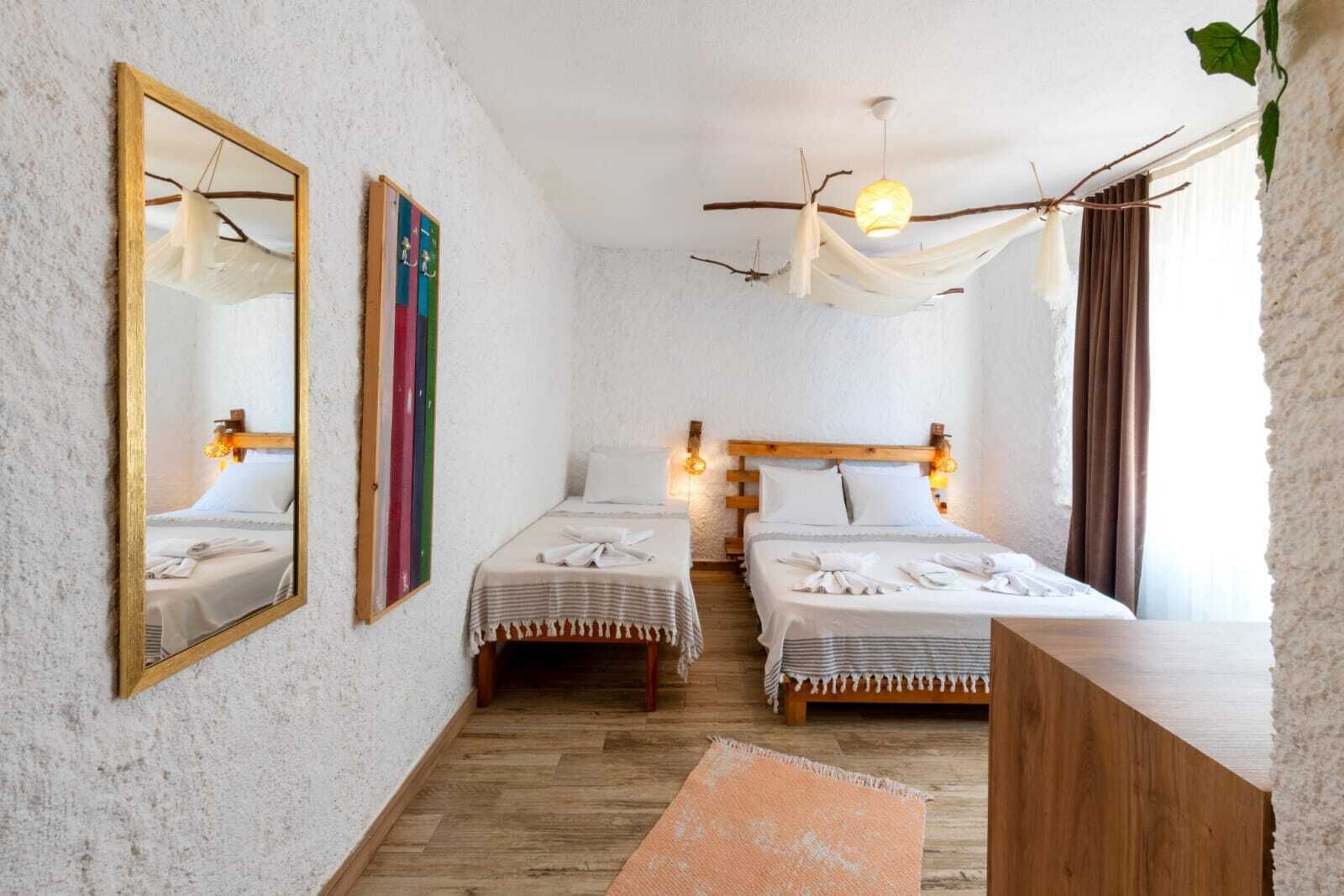 A room with two beds, a wooden bench, a mirror, and a hanging light fixture.