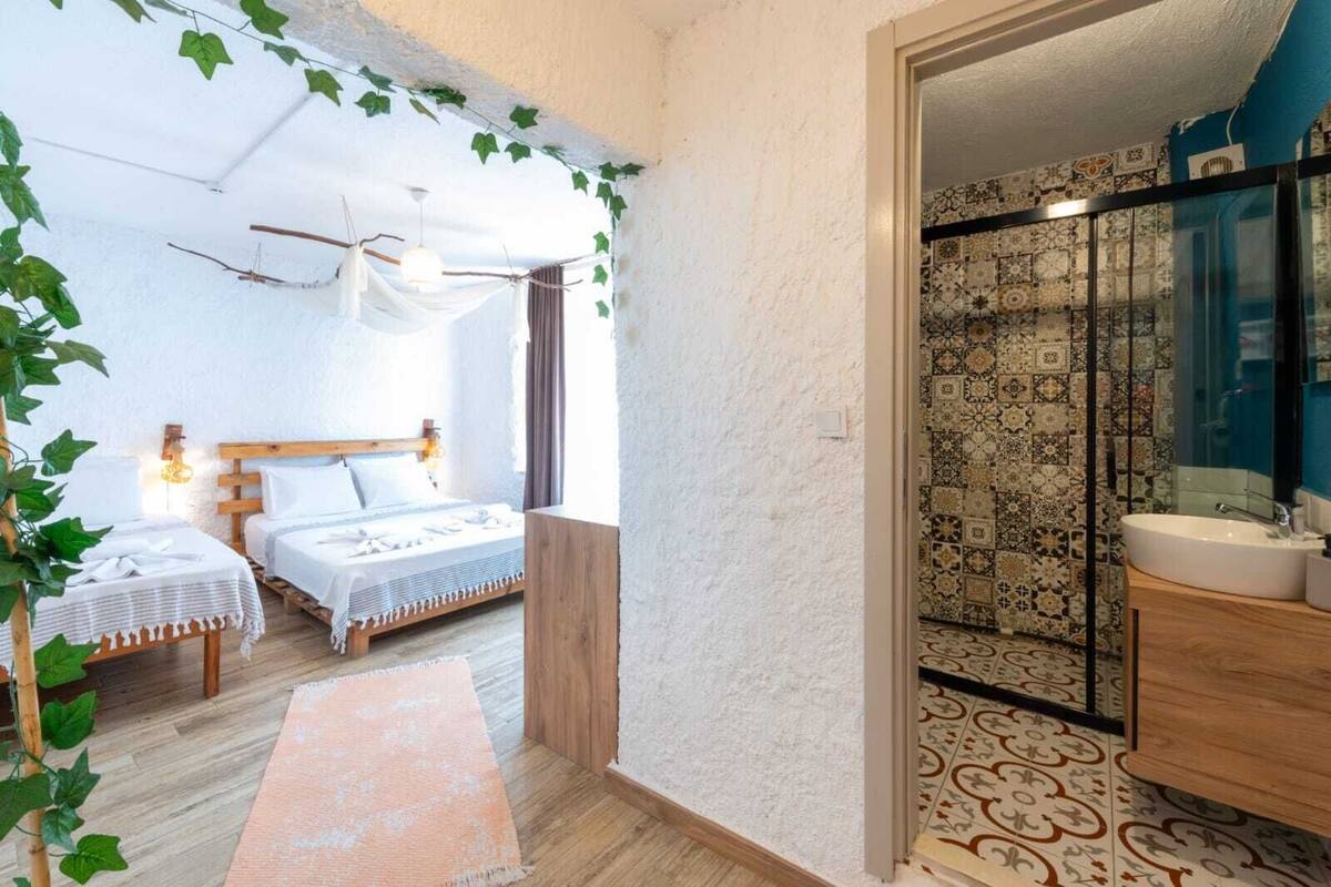 A bedroom with two beds, a wooden floor, a hanging light fixture, and a view of the bathroom with patterned tiles.