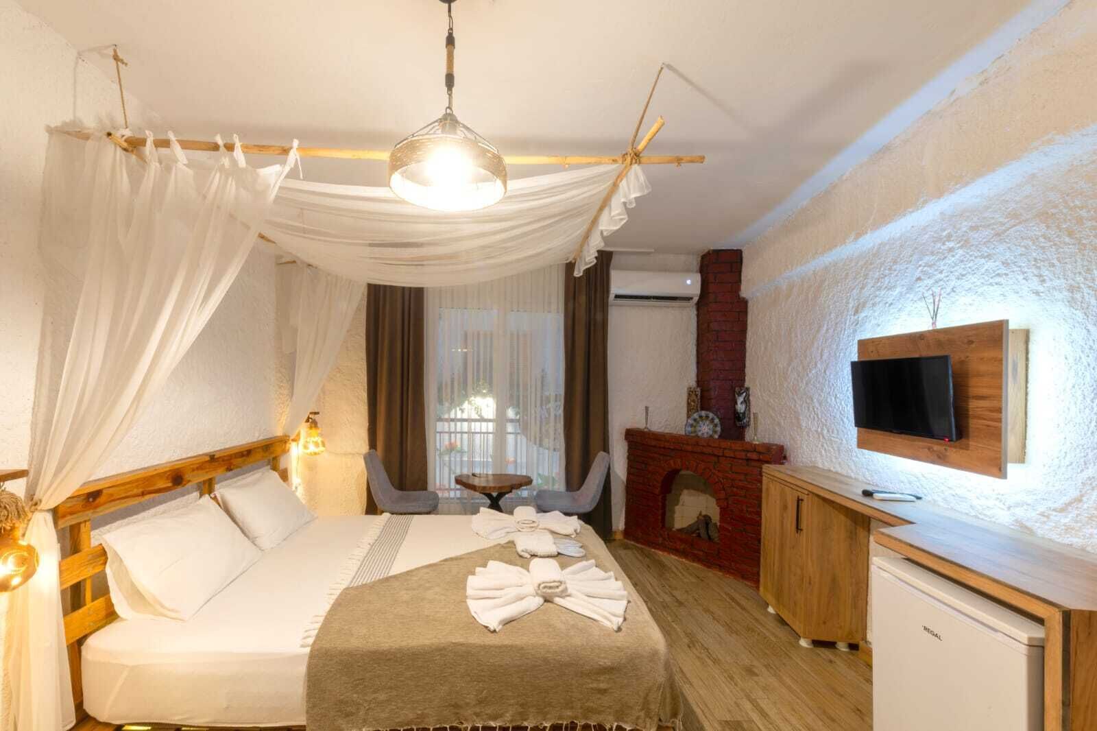 Hotellihuone, jossa on sänky, seinälle asennettu televisio, takka ja työpöytä.