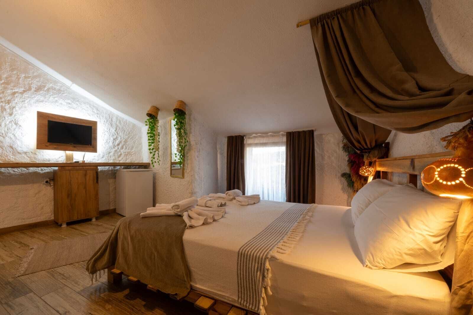Quarto com cama, televisão, cómoda de madeira e janela com cortinas.