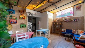 Una sala de estar acogedora con un sofá azul, una mesa de comedor con mantel de lunares y una estantería llena de libros y objetos decorativos.