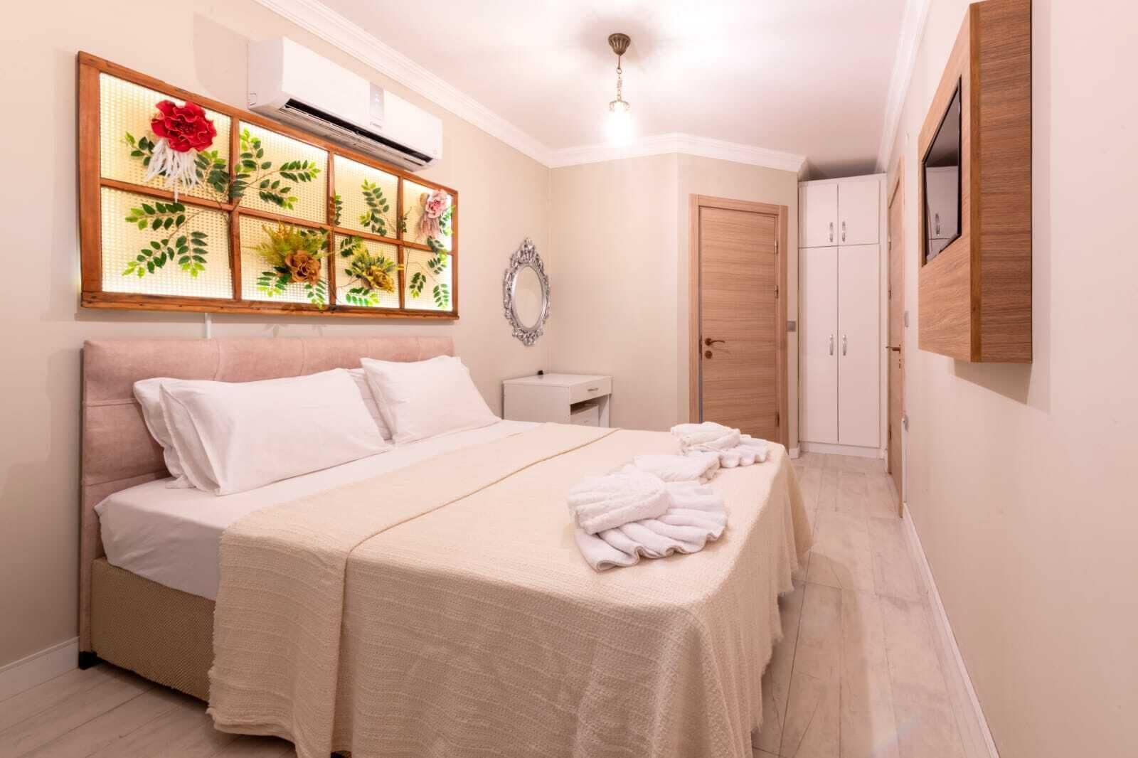 A hotel room with a bed, a bedside table, a mirror, a wardrobe, and a wall-mounted air conditioning unit.
