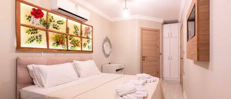 A hotel room with a bed, a bedside table, a mirror, a wardrobe, and a wall-mounted air conditioning unit.