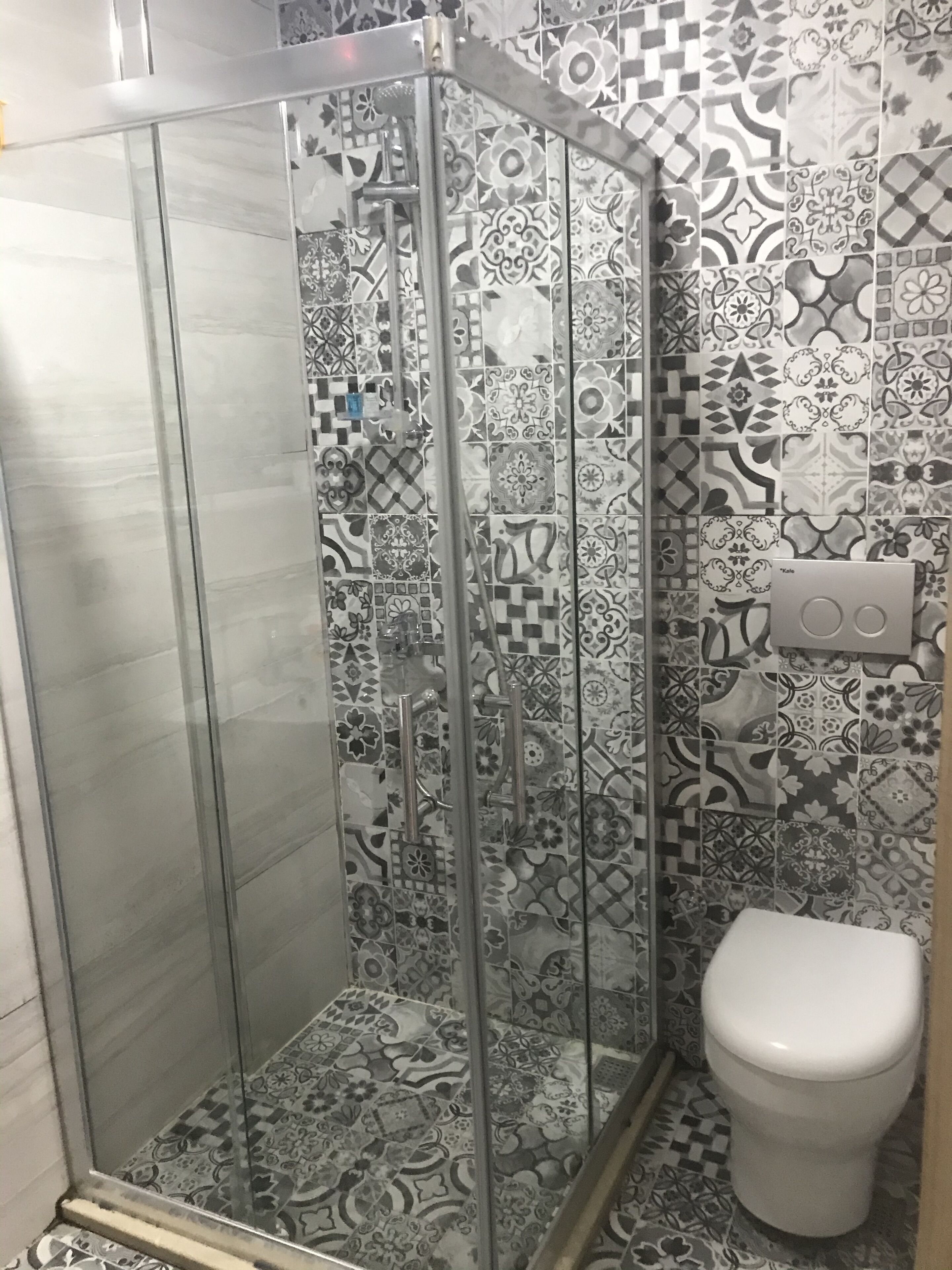 A bathroom with a shower enclosure, patterned tiles, and a toilet.