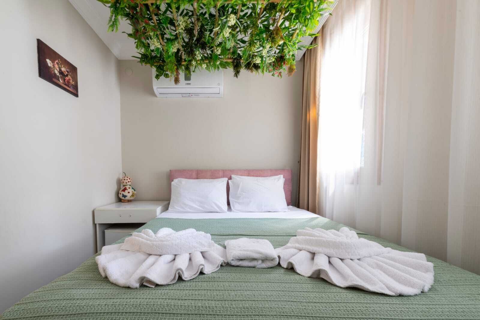Habitación de hotel con cama, mesita de noche, aire acondicionado instalado en la pared y planta colgante.
