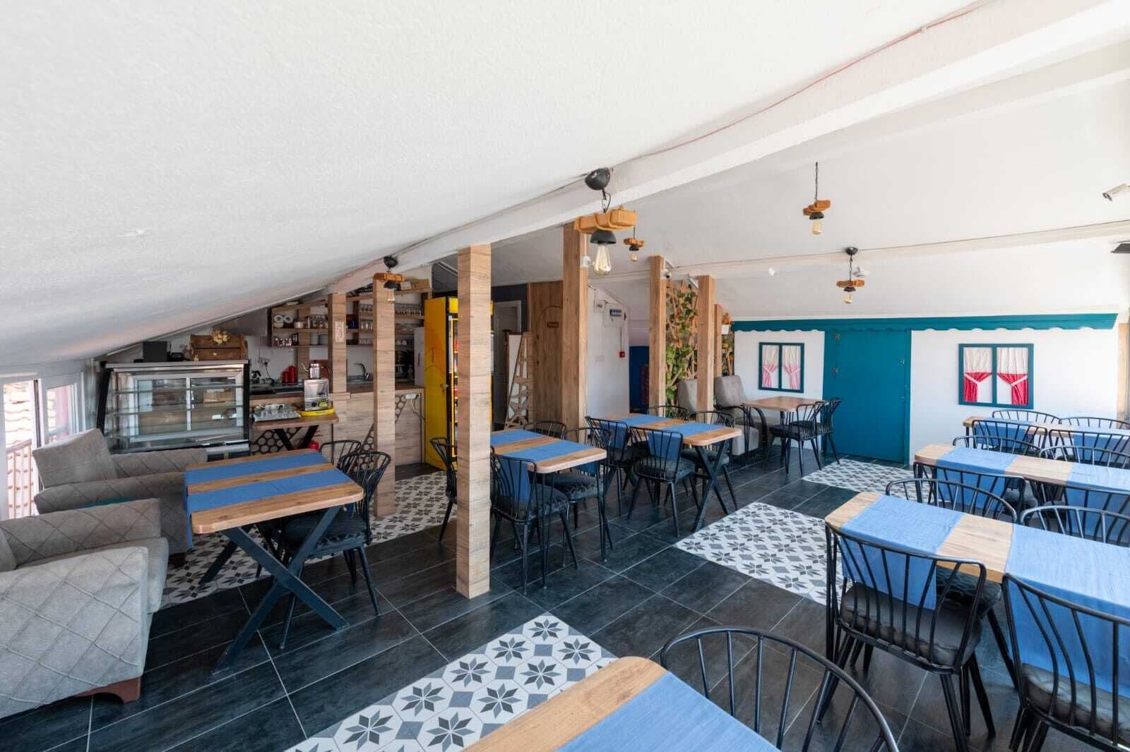 A cozy restaurant with wooden tables and chairs, a kitchen area, and a seating area with a view of the outdoors.