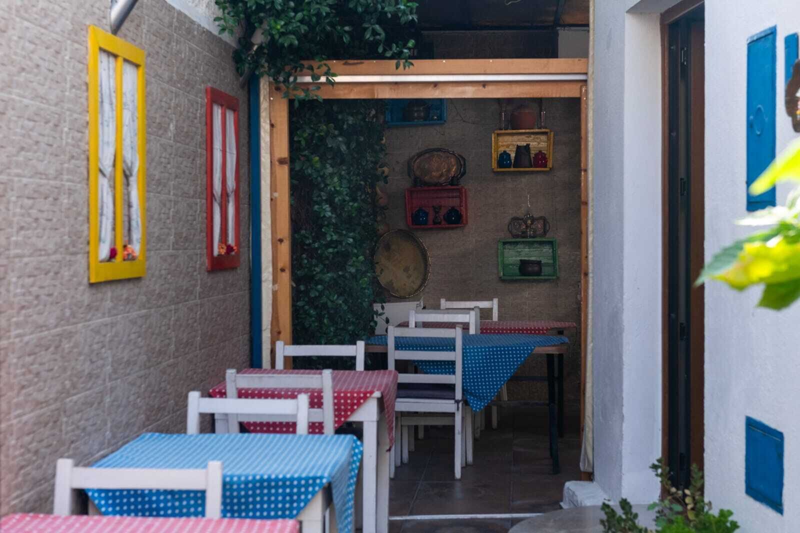 Un estrecho patio al aire libre con mesas y sillas, una puerta de madera y varios adornos en las paredes.