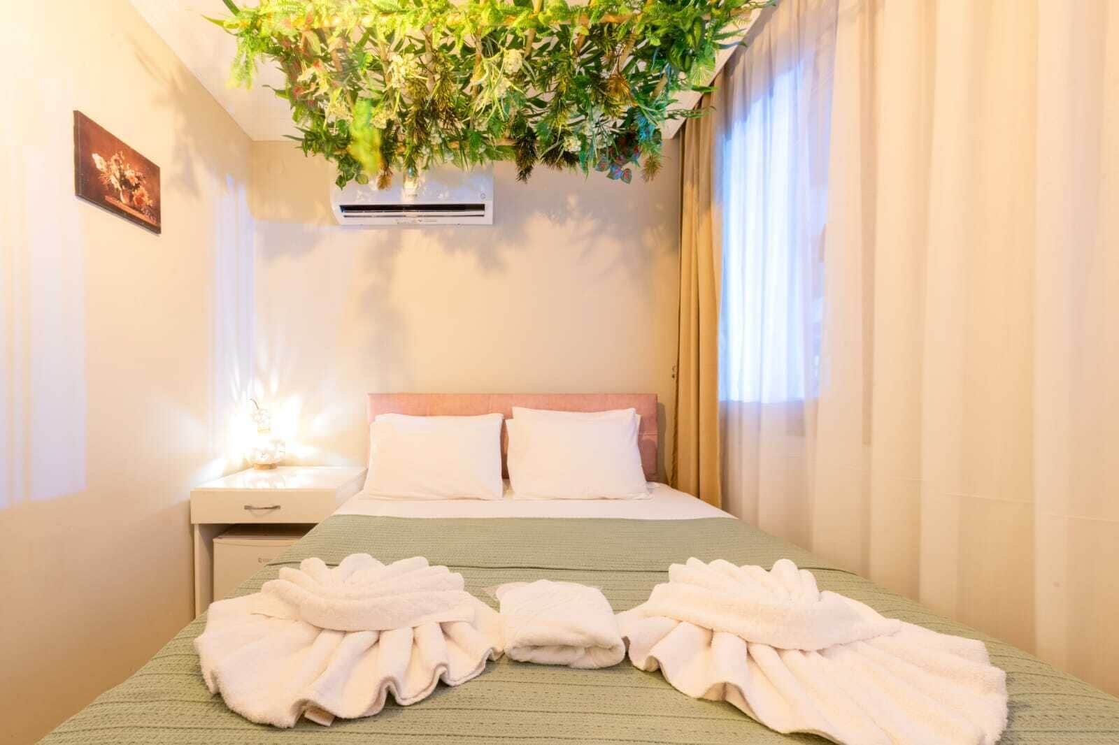 Habitación de hotel con cama, dos almohadas, mesita de noche, aire acondicionado montado en la pared y una planta colgante.