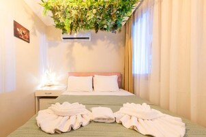Habitación de hotel con cama, dos almohadas, mesita de noche, aire acondicionado montado en la pared y una planta colgante.