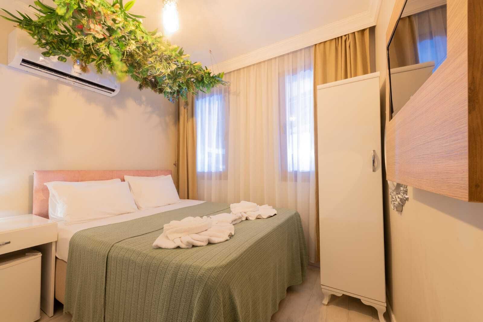 Una habitación de hotel con cama, mesita de noche, armario y planta colgante.