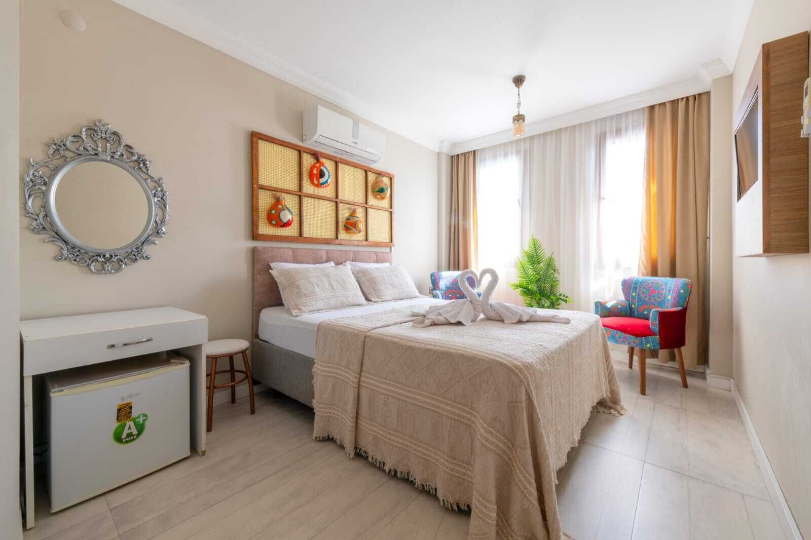 A hotel room with a bed, a desk, a mirror, a decorative wall panel, a window with curtains, and a chair.