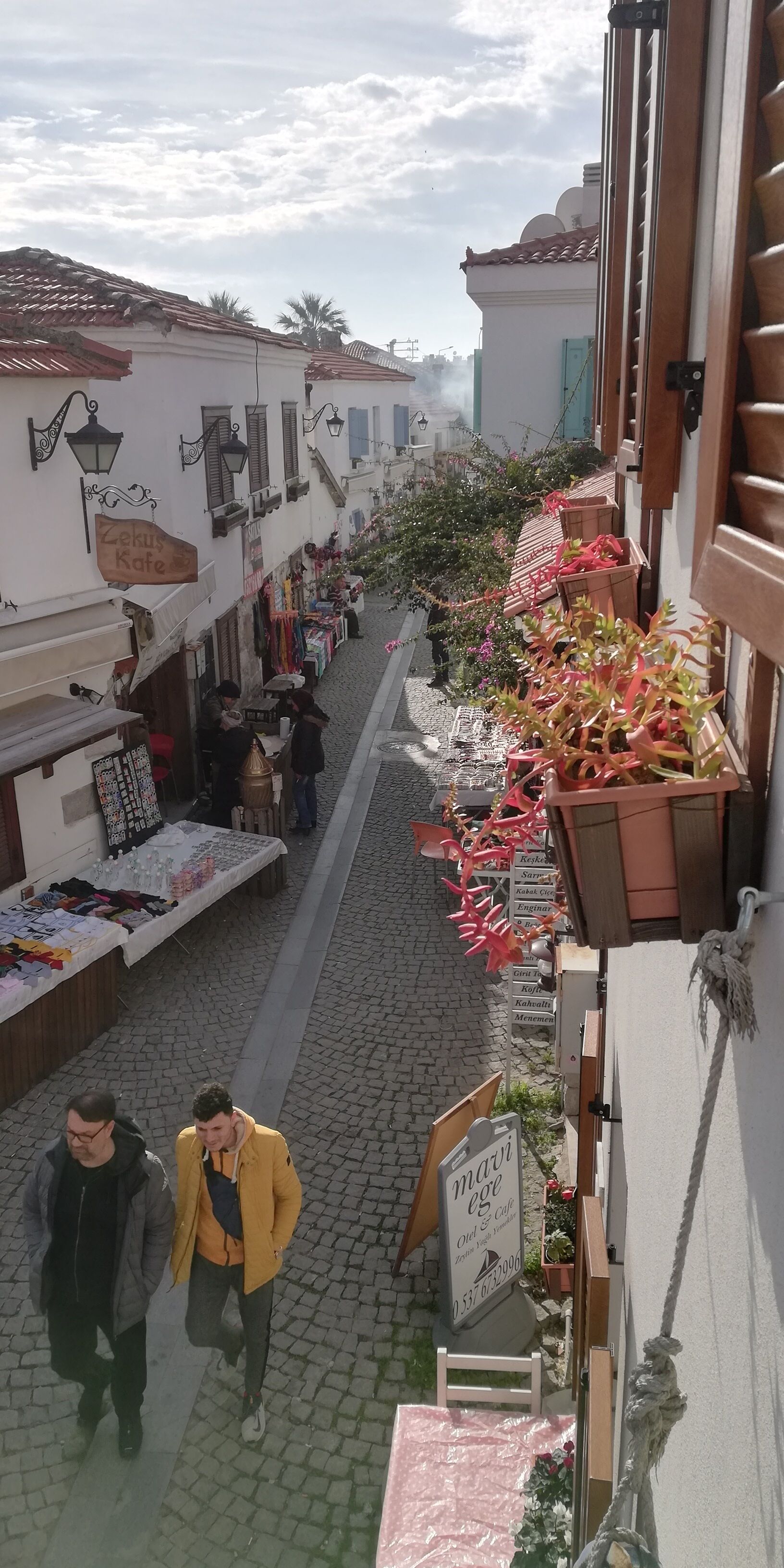 Una stretta strada acciottolata fiancheggiata da negozi e balconi decorati con fiori.
