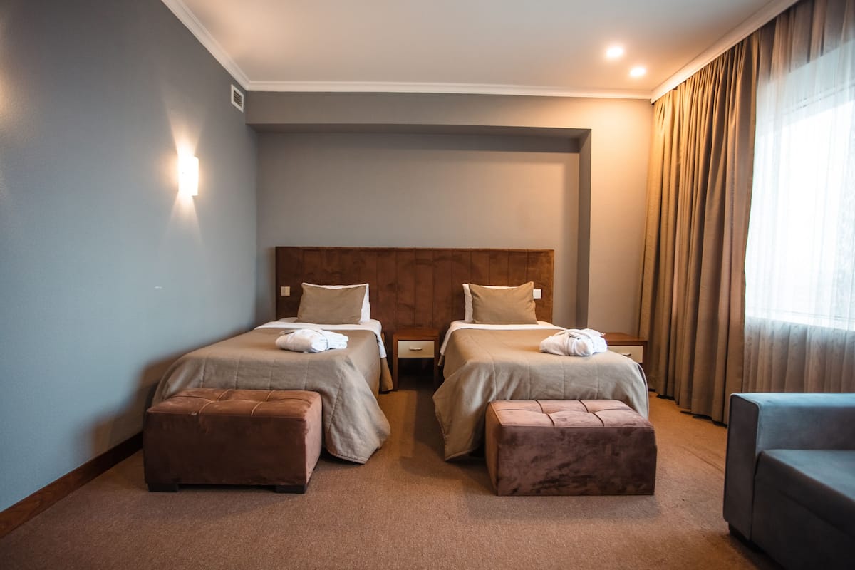A hotel room with two beds, a wooden headboard, a small table, and a chair.