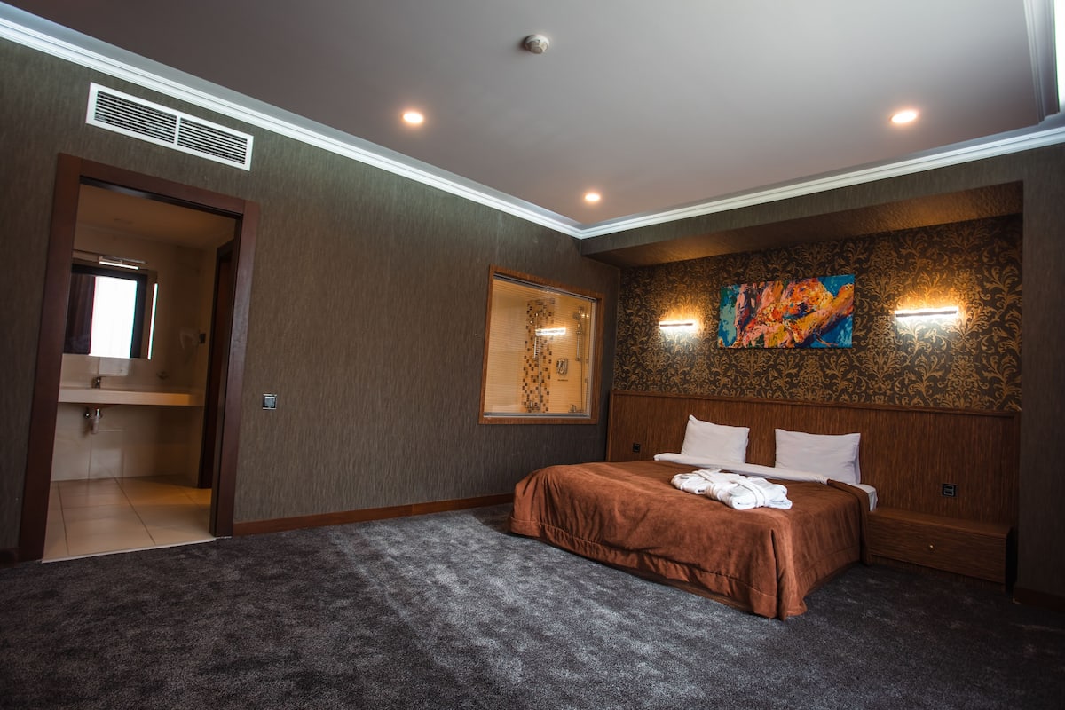 A bedroom with a large bed, a painting on the wall, and a window.