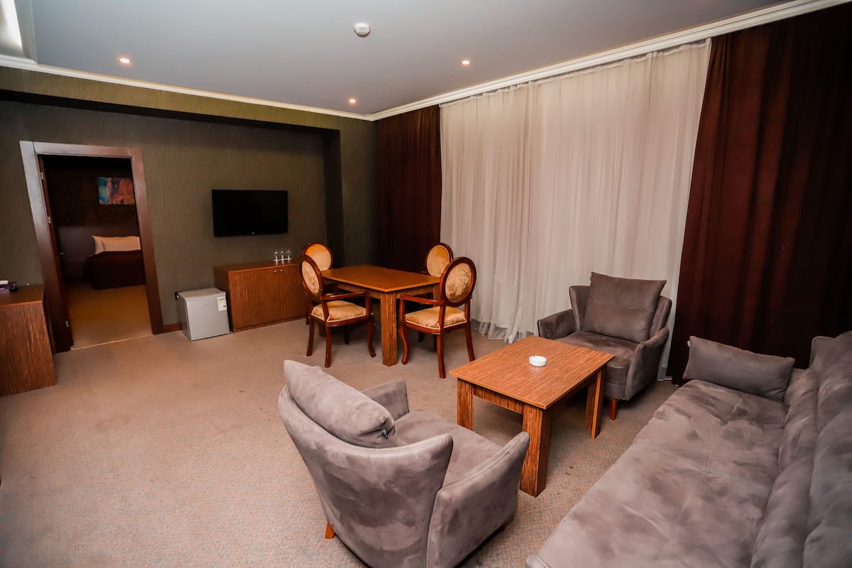 A modern living room with a sofa, armchairs, a dining table, and a TV mounted on the wall.